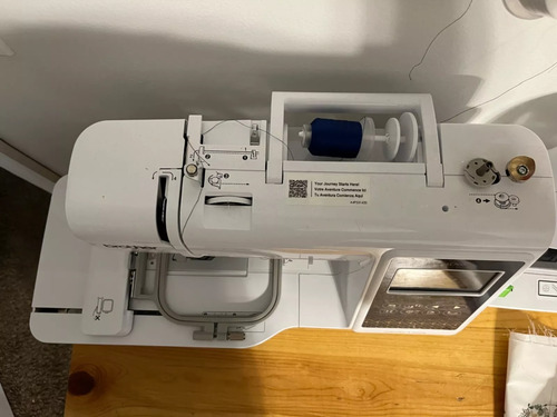 Top-view of Brother SE700 sewing machine—thread spool, upper threading path, 4×4 hoop, and LCD screen visible on wooden table.